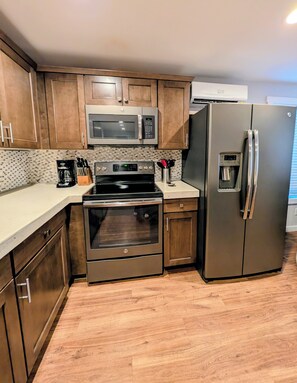 A kitchen with wooden cabinets, a stainless steel refrigerator, a microwave, an oven, and a coffee maker. - Patio Beach Retreat · Walk to Lake. 2 Bedroom, 1 Bath. Enjoy stair-free living, a full kitchen, private patio with grill, sun loungers, and easy access to Slidewaters, wineries, and downtown Chelan. (Chelan)