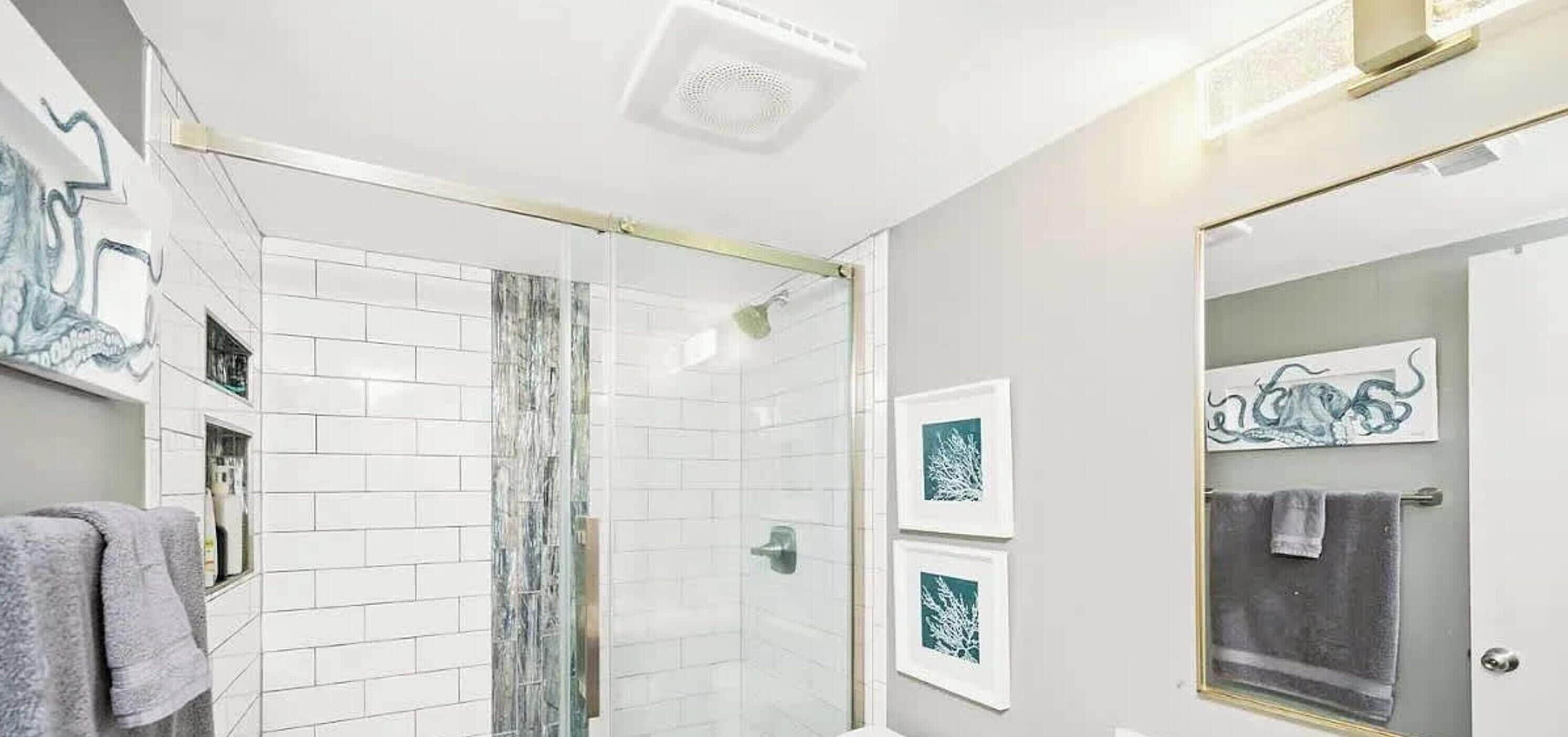 A modern bathroom with white tiles, a glass shower enclosure, and framed artwork on the walls.