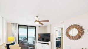 Una habitación de hotel con balcón, ventilador de techo, televisión y espejo decorativo.