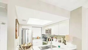 Una cocina moderna con armarios blancos, un refrigerador de acero inoxidable y un microondas.