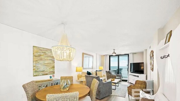 Una sala de estar luminosa y moderna con una araña, muebles de mimbre, un televisor de pantalla plana y un balcón con vistas.