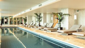 Ein langer, überdachter Schwimmbereich mit Liegestühlen und Kübelpflanzen an den Seiten.