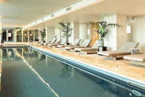 Ein langer, überdachter Schwimmbereich mit Liegestühlen und Kübelpflanzen an den Seiten.