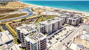 Ein moderner Wohnkomplex mit mehreren Gebäuden, einem Parkplatz und einem Strand im Hintergrund.
