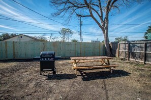 A backyard with a barbecue grill, a picnic table, and a wooden fence. - Sleeps 22 - Seaside Escape Two Fully Remodeled Homes for Your Group (Corpus Christi)