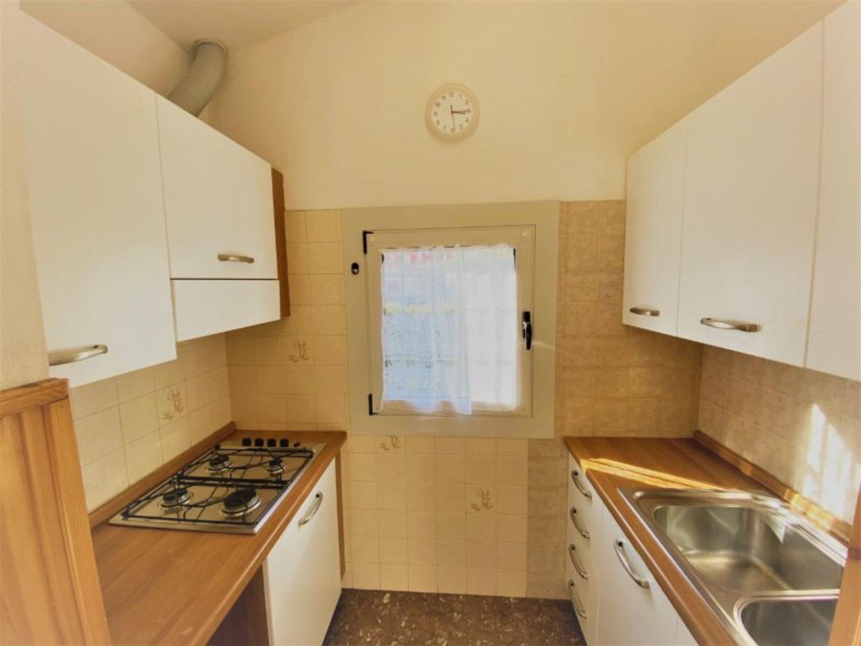 A compact kitchen with white cabinets, a gas stove, a sink, and a small window with a curtain.