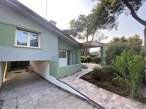 Ein modernes Haus mit Flachdach, überdachter Veranda und einem kleinen Garten.