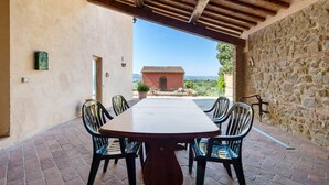 Un patio al aire libre con una mesa y sillas de madera, un muro de piedra y vistas a un edificio distante.
