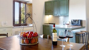 Una cocina con una mesa de comedor, una cesta de frutas, una botella de vino y dos copas de vino.