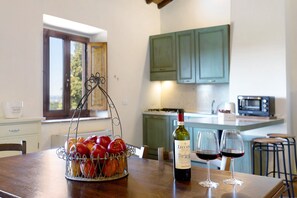 Una cocina con una mesa de comedor, una cesta de frutas, una botella de vino y dos copas de vino.