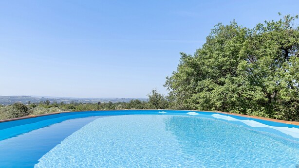 Piscina azul cristalina con vistas a árboles y un paisaje lejano.