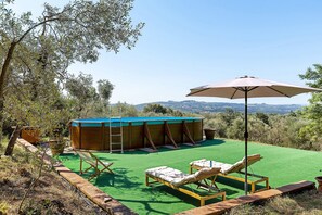 Una piscina exterior con vistas al paisaje, rodeada de sillones de descanso y un gran paraguas.