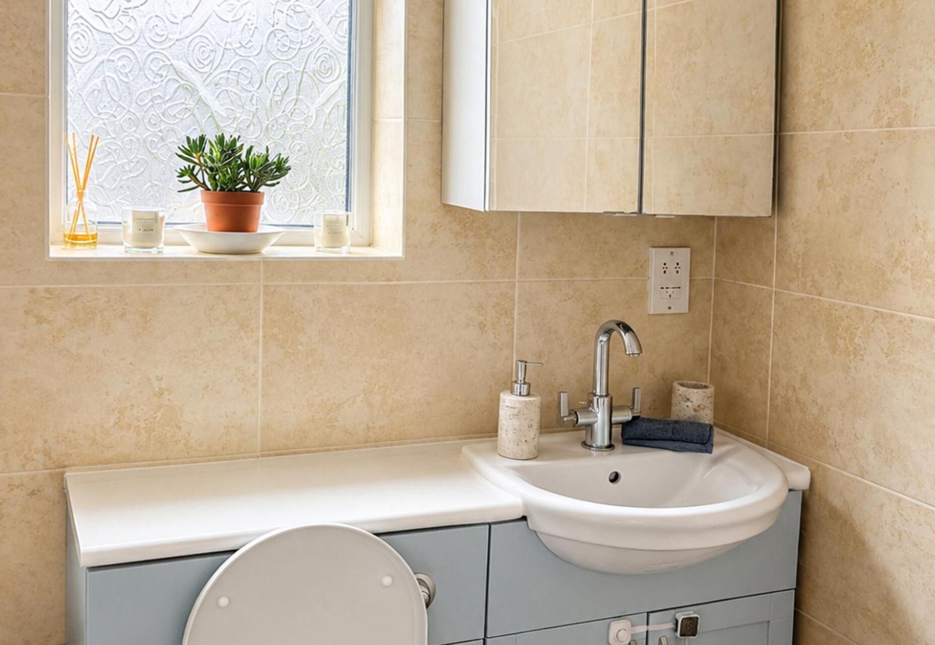 Un baño con lavamanos, inodoro, ventana y una planta en maceta en el alféizar.