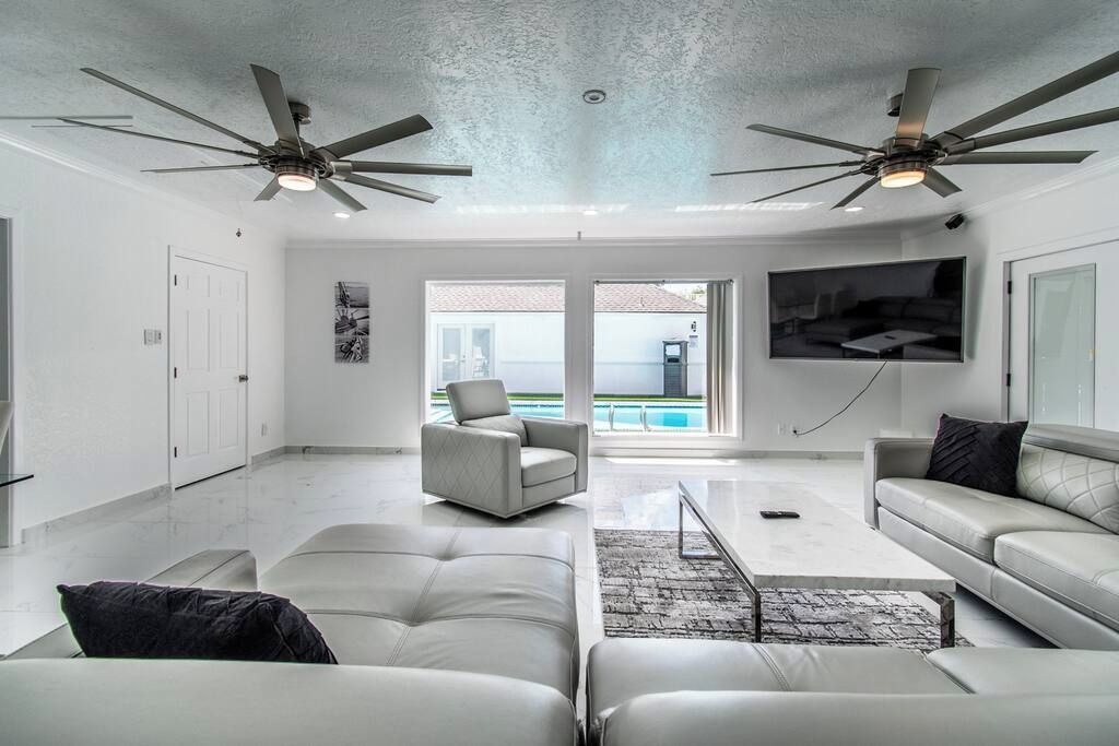 A spacious living room with a large TV, ceiling fans, and a view of the outdoors.
