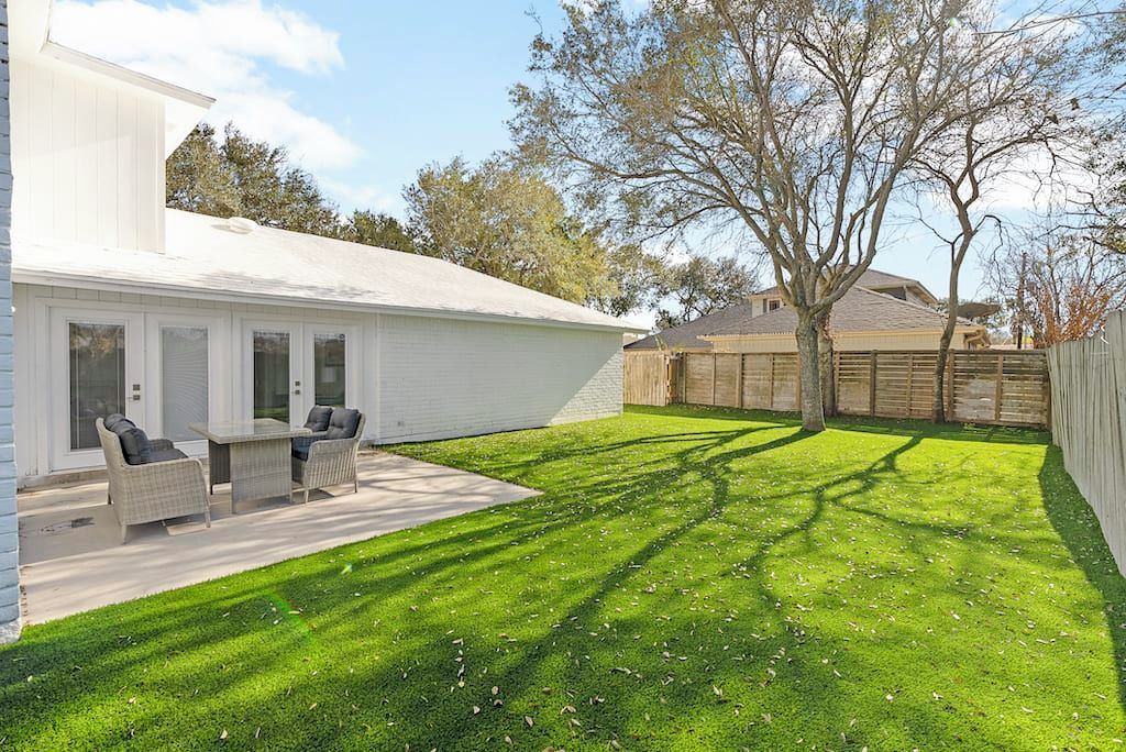 A white house with a patio, a lawn, and a wooden fence.