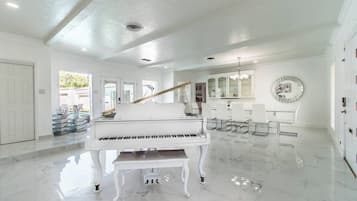 Una habitación espaciosa con un piano de cola, un comedor con sillas y una cocina con armarios.