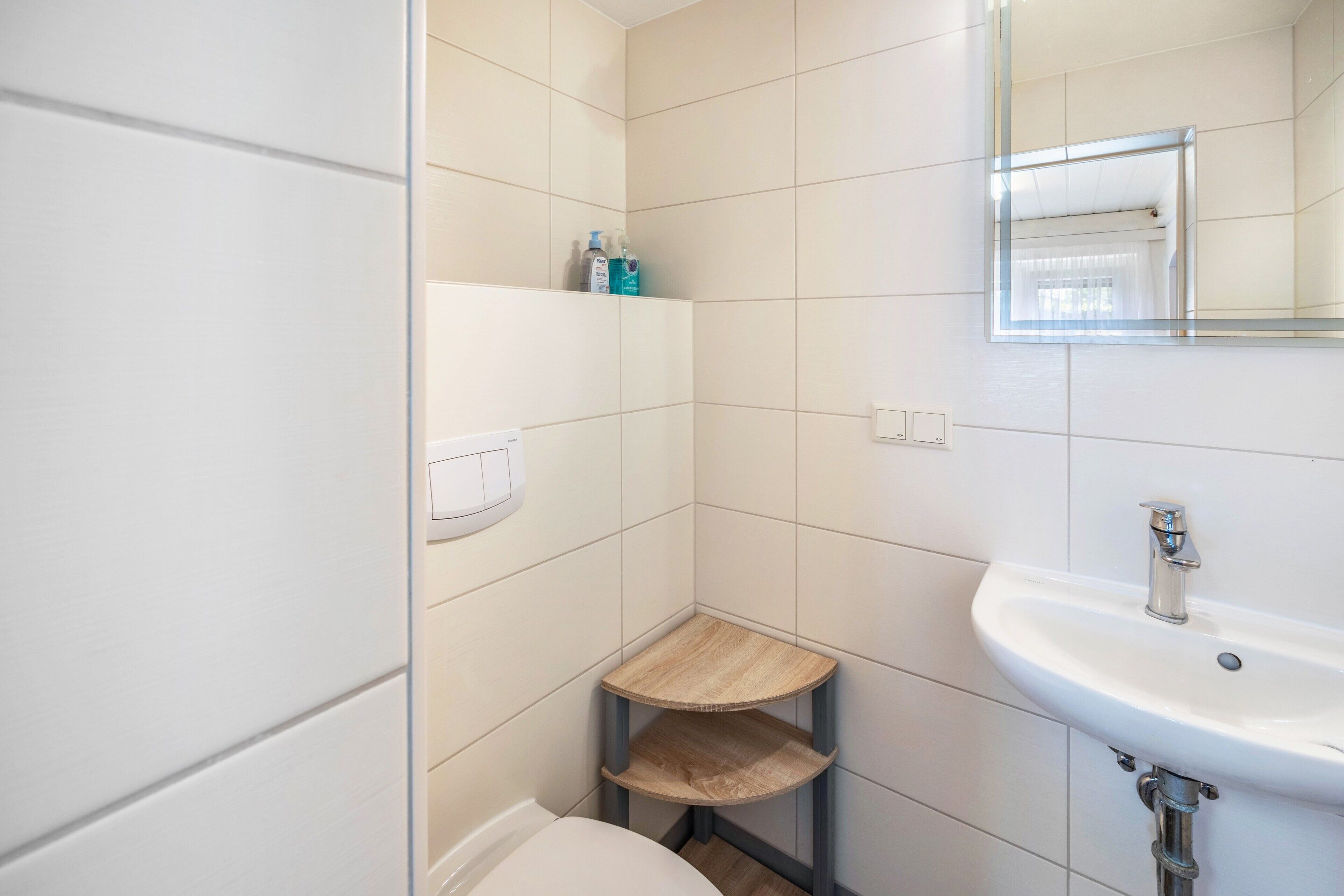 A bathroom with a white sink, a mirror, and a small wooden shelf.