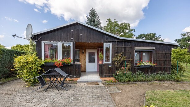 A wooden house with a paved entrance, a satellite dish, and potted plants.