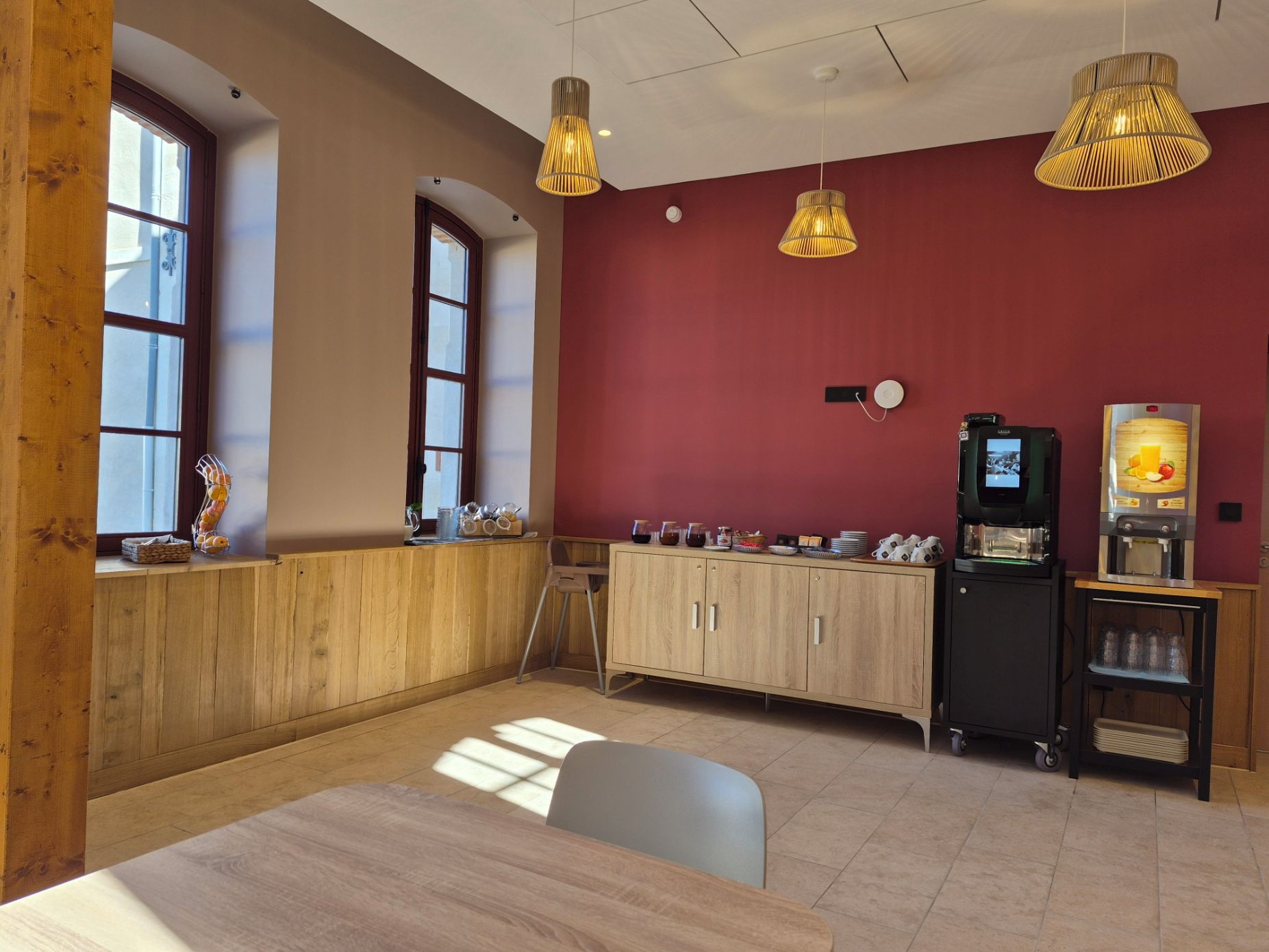 A modern cafe with wooden furniture, a red accent wall, and pendant lighting.