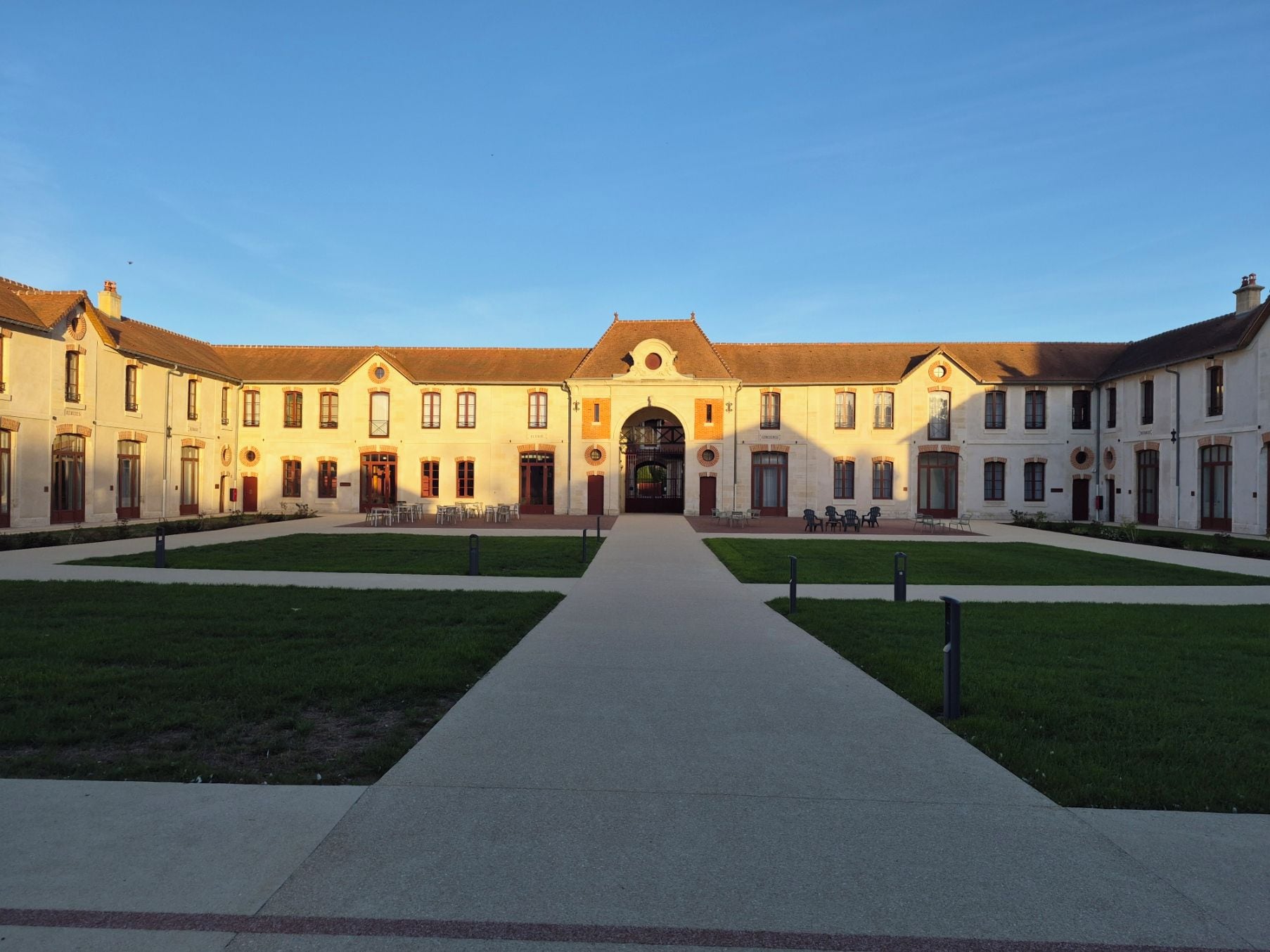 A courtyard with a central pathway leading to a building with a symmetrical facade, multiple windows, and a central archway.