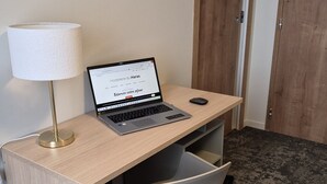 Una laptop sobre un escritorio con una lámpara, una silla y una puerta al fondo.
