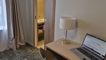 Habitación de hotel con escritorio, una computadora portátil, lámpara y baño visible a través de una puerta abierta.