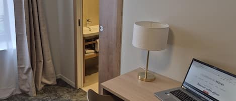 A hotel room with a desk, a laptop, a lamp, and a bathroom visible through an open door.