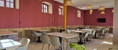 A spacious dining area with multiple tables and chairs, wooden beams, and pendant lighting.