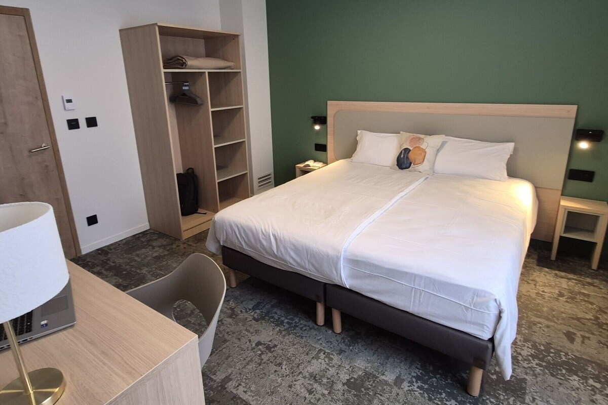Habitación de hotel con cama, escritorio, silla, armario y mesita de noche.