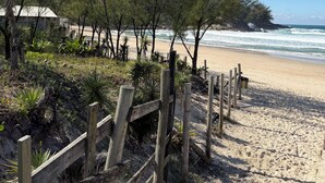 Ein Strand mit Holzzaun, viel Grün und freiem Blick auf das Meer.
