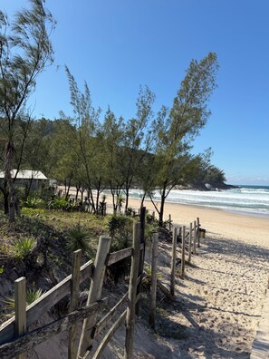 Ein Strand mit Holzzaun, viel Grün und freiem Blick auf das Meer.