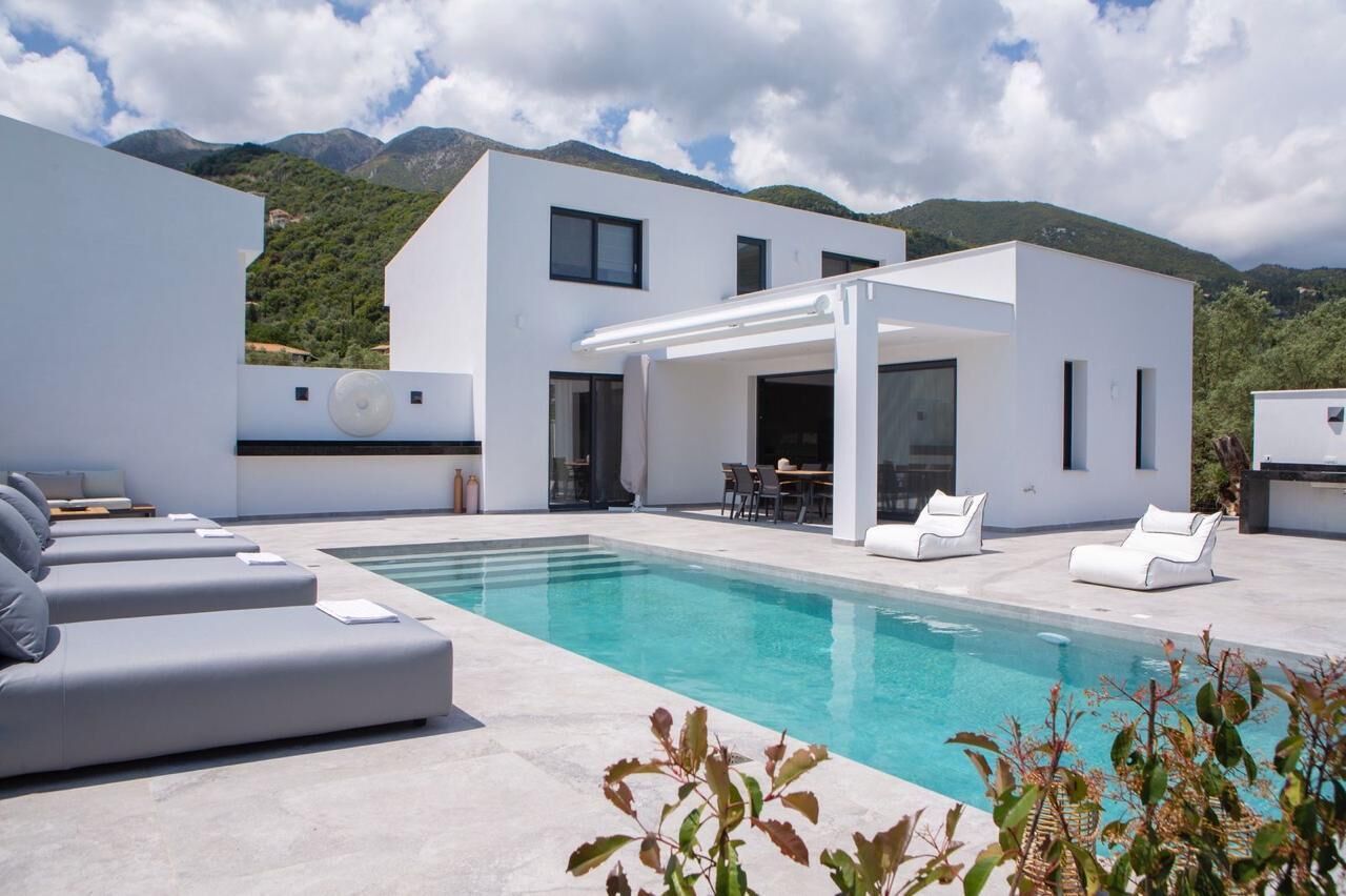 A modern poolside area with a pool, white walls, and a mountain backdrop.