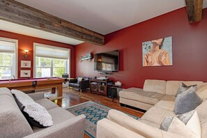 Un salon avec une table de billard, un canapé, un téléviseur et des œuvres d’art accrochées au mur.