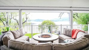 A covered outdoor seating area with wicker furniture, a round table, and a fire pit. - Spacious 4-bedroom home with private beach,  dock, large yard, outdoor shower. (Kelowna)