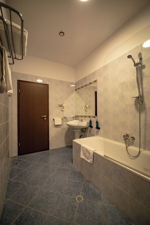 A bathroom with a shower, sink, and bathtub, featuring blue tiles and a wooden door. - HOTEL AURELIA (Giroc)