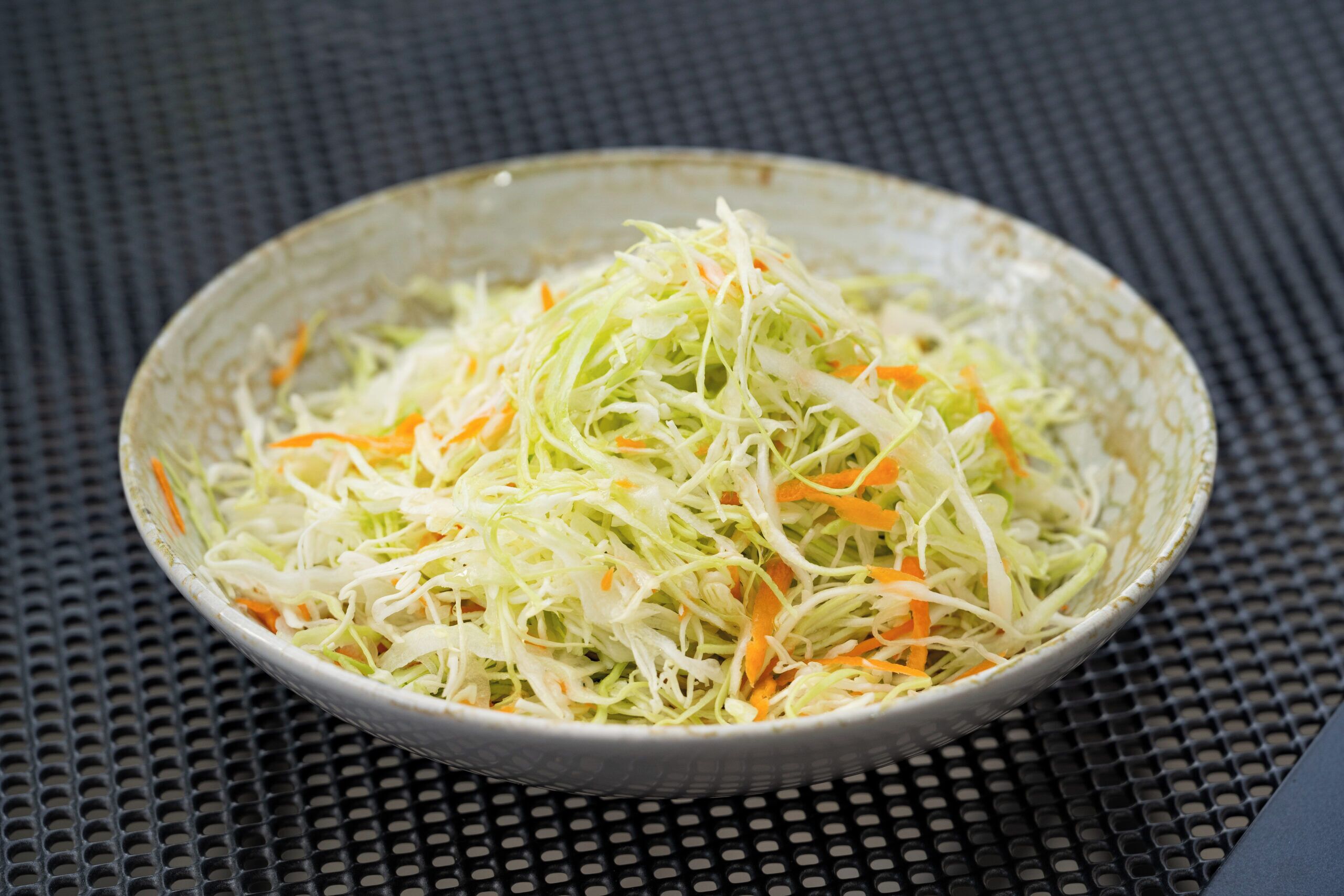 Un plato de ensalada de col sobre una superficie texturizada.