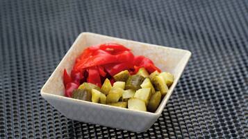 A square ceramic bowl with diced pickles and red peppers on a textured surface.