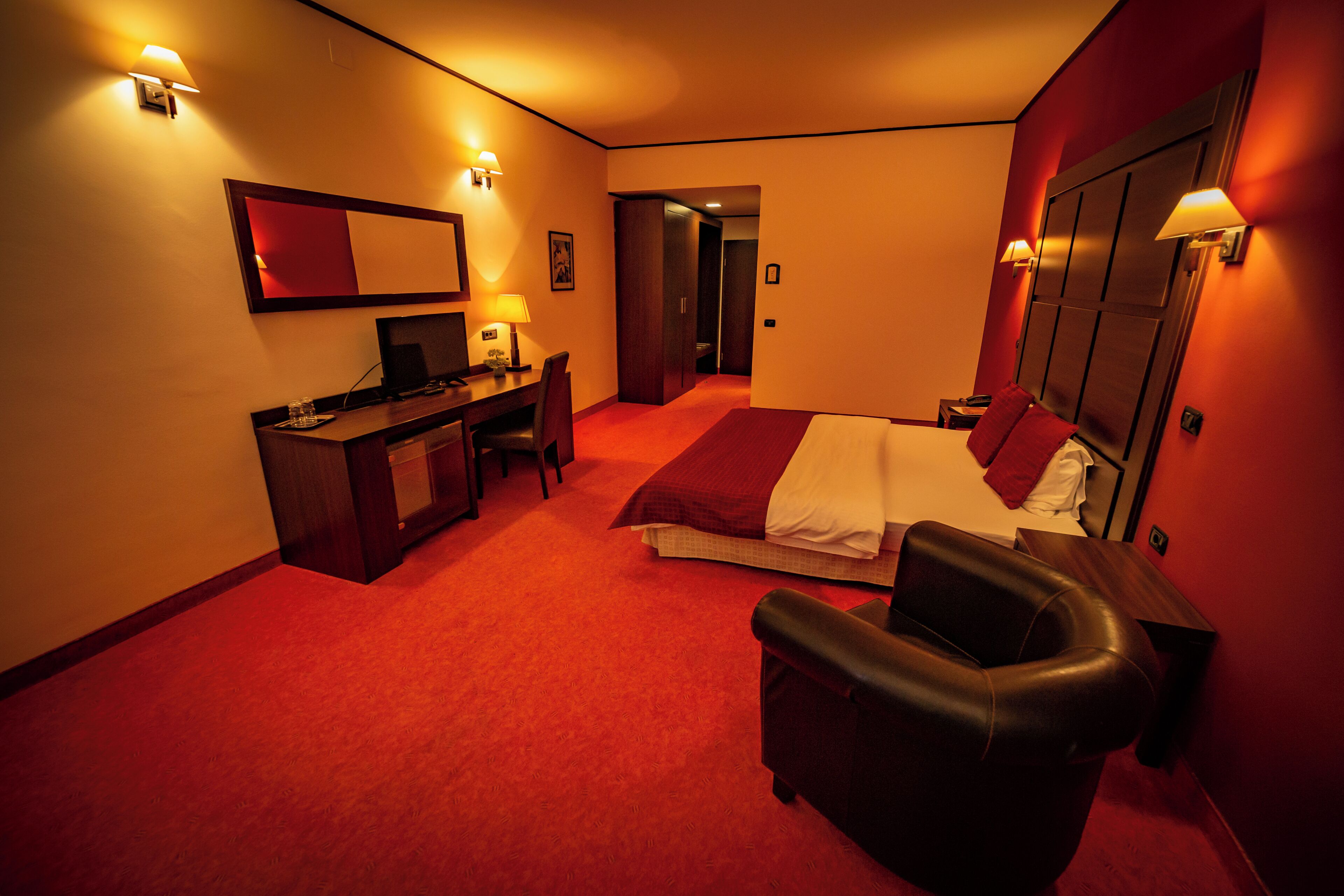 A hotel room with a bed, desk, chair, and a mirror.