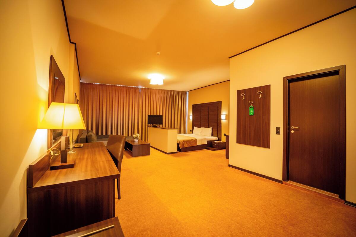 A hotel room with a bed, bedside table, lamp, and a desk with a chair.