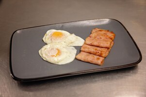 Un plato con dos huevos fritos y tres lonchas de jamón sobre un plato rectangular.