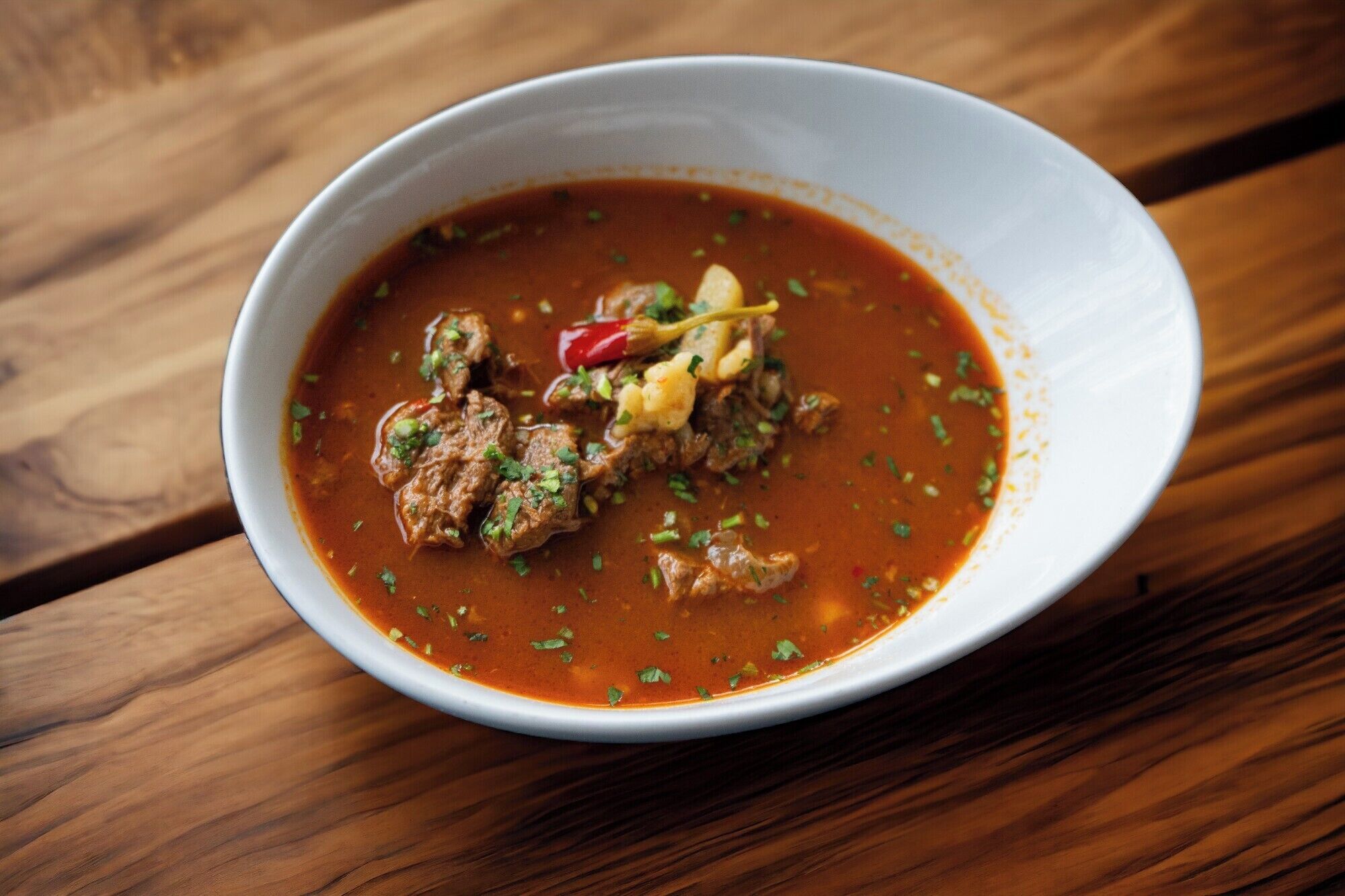 A bowl of stew with meat and vegetables on a wooden table.