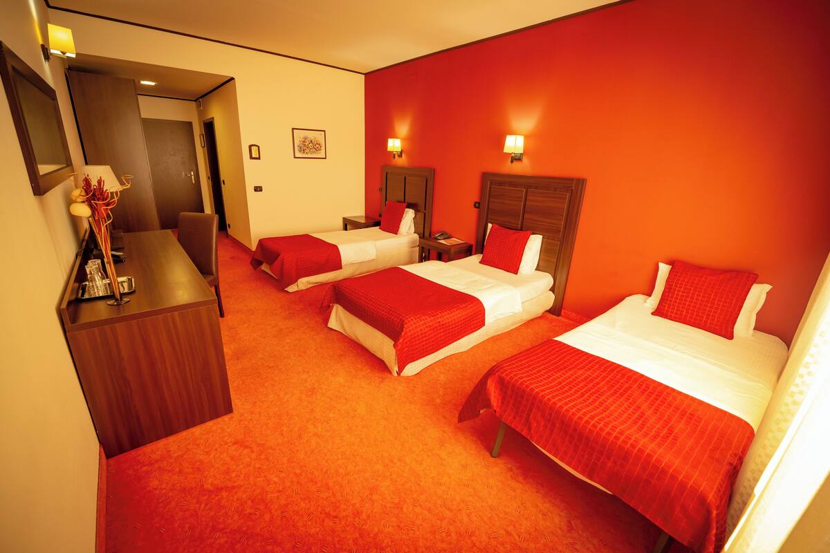 A hotel room with three beds, a desk, and a mirror.