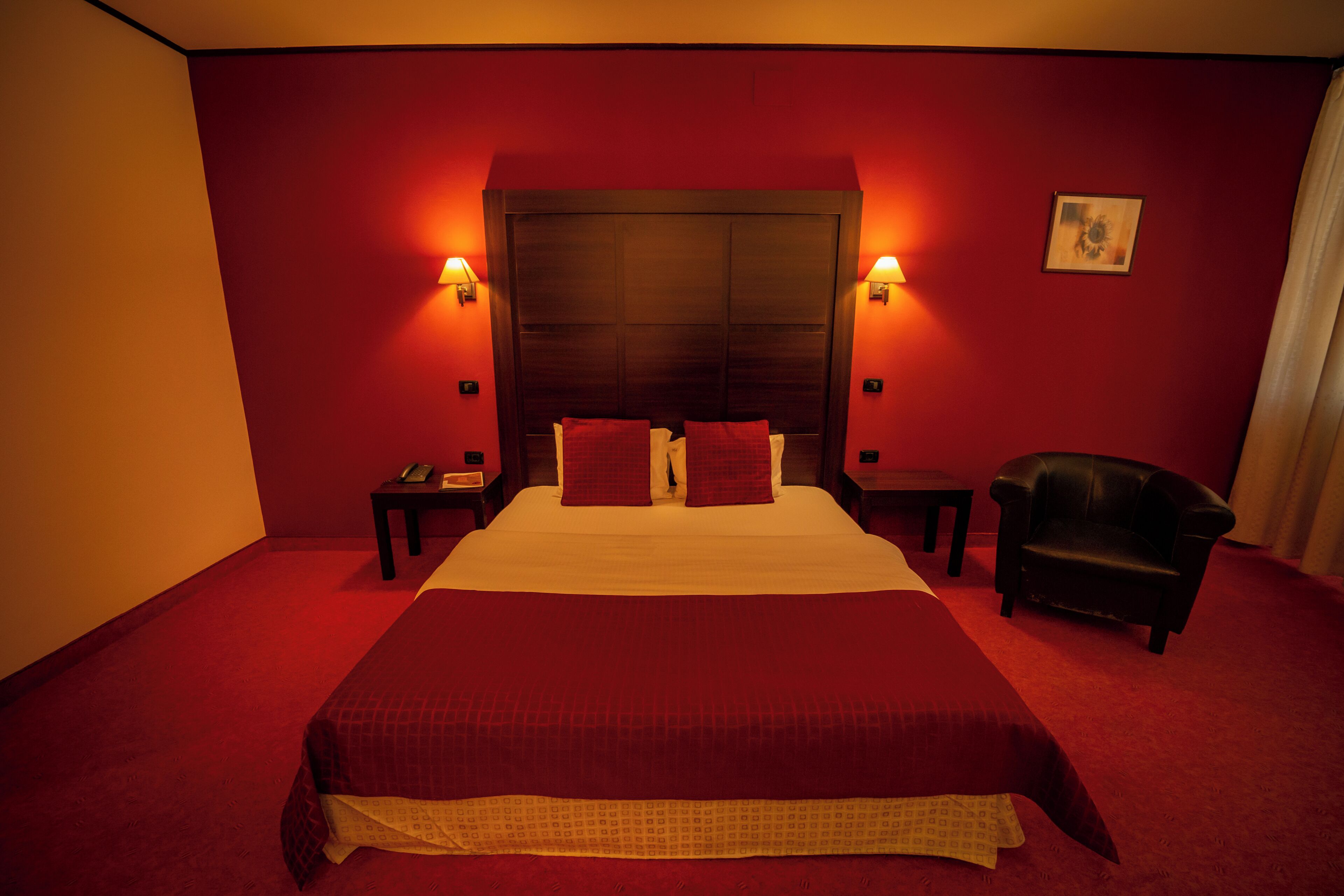 Una habitación de hotel con una cama grande, dos mesitas de noche, una silla y paredes rojas.