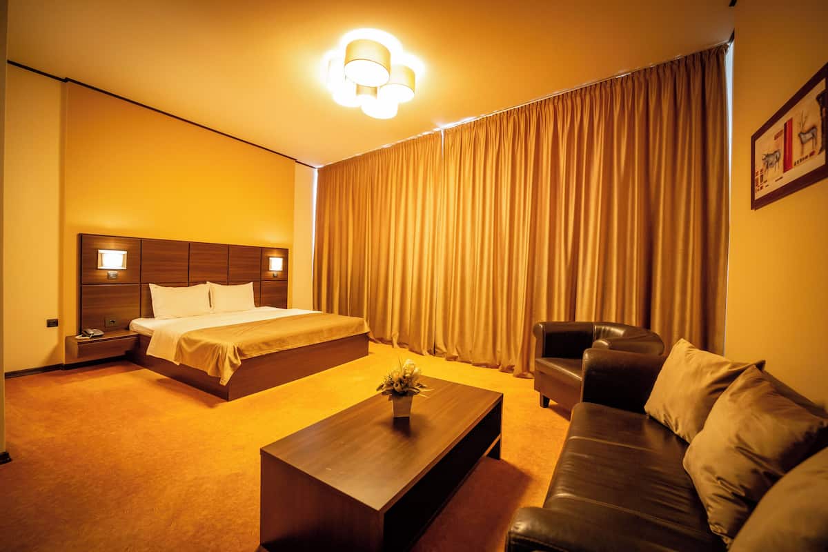 A hotel room with a bed, a sofa, a coffee table, and a curtain.