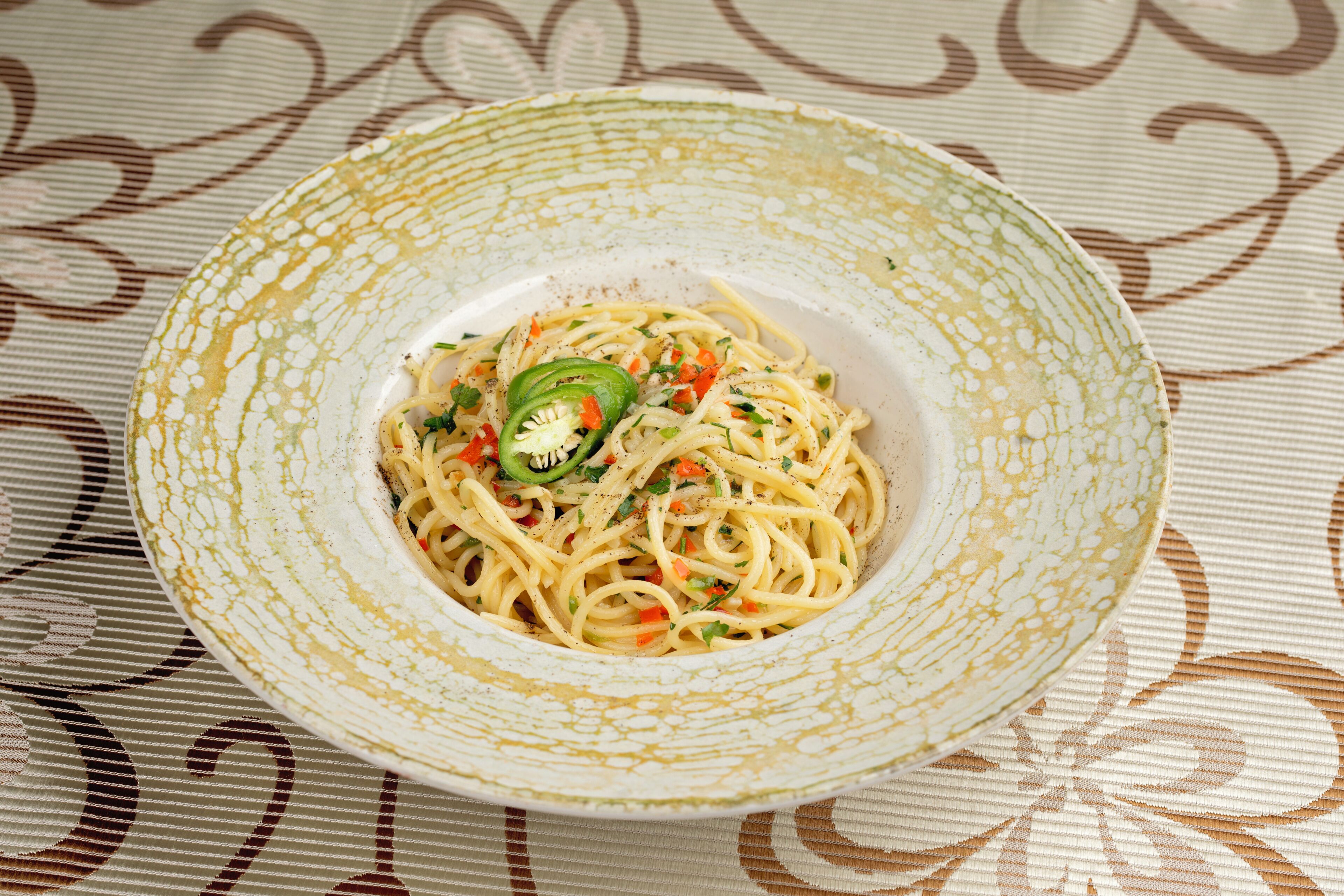 A bowl of pasta with vegetables on a patterned tablecloth.