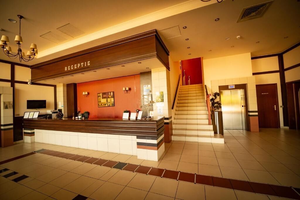 Zona de recepción de hotel con mostrador, escalera y televisor montado en la pared.