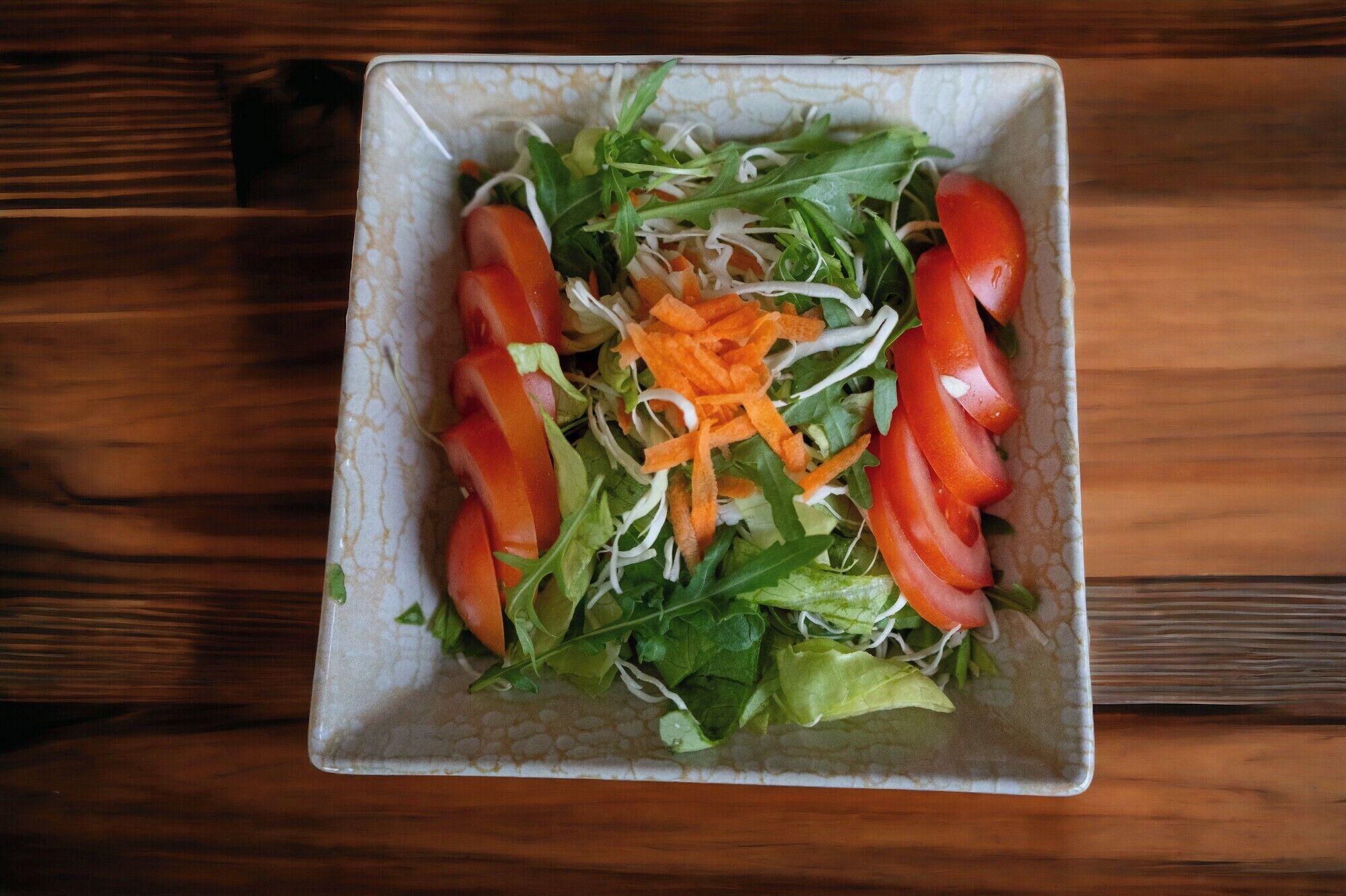 Une assiette carrée avec une salade, posée sur une table en bois.
