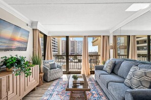 Ein modernes Wohnzimmer mit großem Fernseher, bequemen Sitzmöglichkeiten, einem gemusterten Teppich und Blick auf die Stadt.