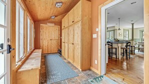 A wooden hallway with built-in benches, a stone-tiled floor, and a view into a kitchen area. - Lakefront 4-BR Retreat Near Okemo (Ludlow)