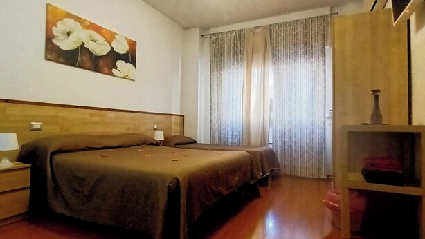 A bedroom with a wooden headboard, two beds, a nightstand with a lamp, a wooden cabinet, and a painting on the wall.